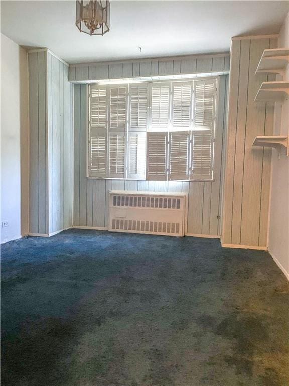 unfurnished room featuring radiator, wood walls, and dark colored carpet