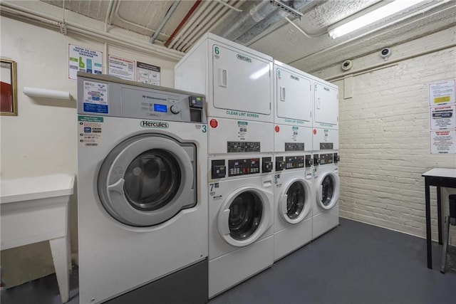 laundry room featuring stacked washer / drying machine, washer and clothes dryer, and brick wall