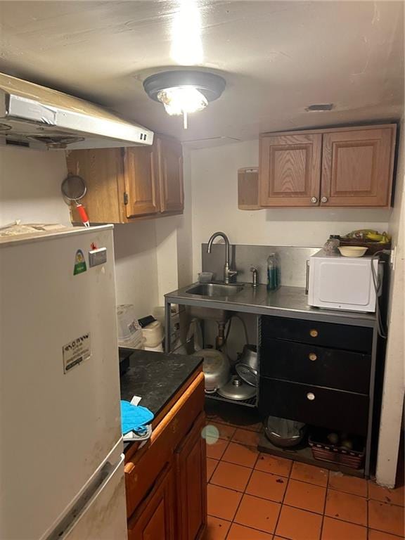 kitchen with freestanding refrigerator, a sink, light tile patterned floors, and brown cabinets