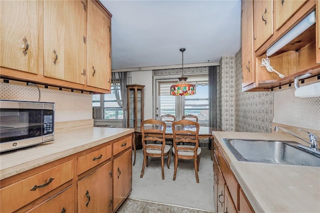 kitchen with light countertops, hanging light fixtures, backsplash, stainless steel microwave, and wallpapered walls