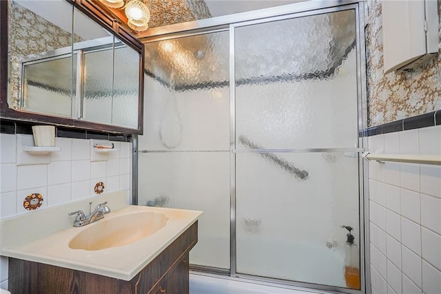 full bath featuring combined bath / shower with glass door, tile walls, vanity, and wallpapered walls