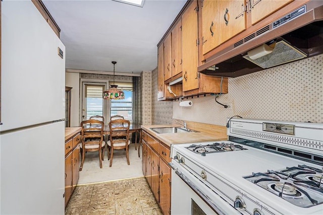 kitchen featuring white appliances, under cabinet range hood, light countertops, and a sink