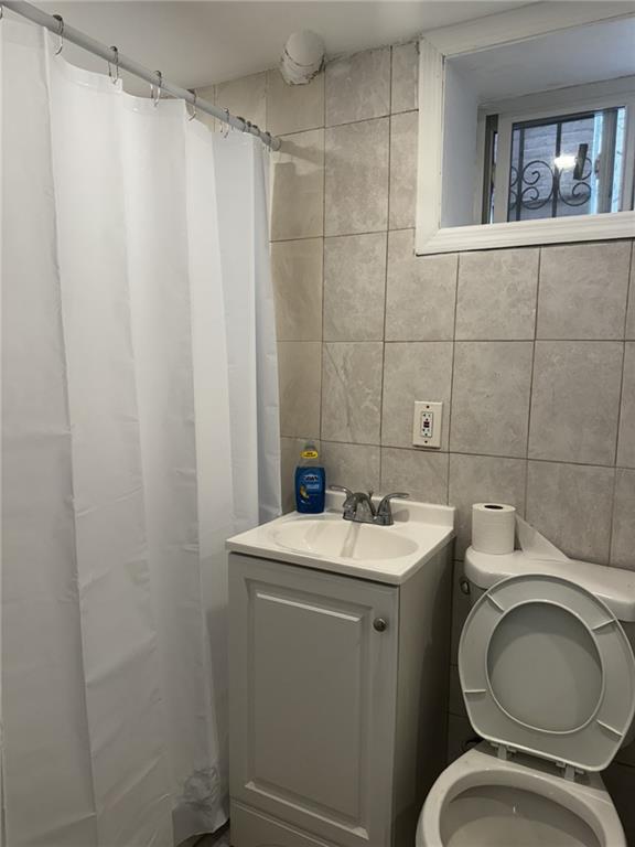 bathroom with tile walls, vanity, curtained shower, and toilet