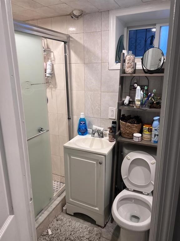 bathroom featuring toilet, an enclosed shower, tile walls, vanity, and tile patterned flooring