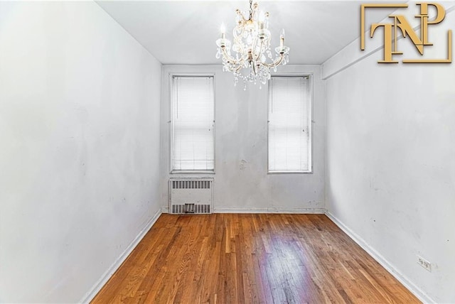 spare room with baseboards, radiator heating unit, wood finished floors, and an inviting chandelier