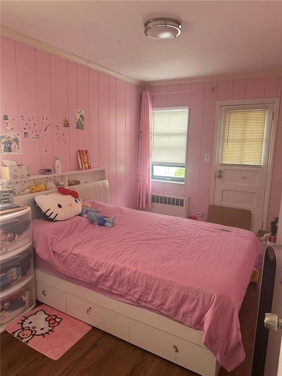 bedroom with wood walls, radiator, and dark hardwood / wood-style flooring