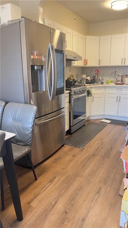 kitchen with under cabinet range hood, stainless steel appliances, white cabinetry, light countertops, and light wood-type flooring