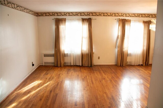 empty room with a healthy amount of sunlight, wood-type flooring, and radiator heating unit