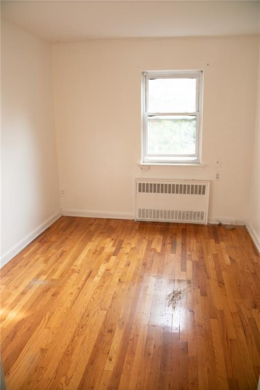 spare room featuring radiator heating unit and light hardwood / wood-style flooring