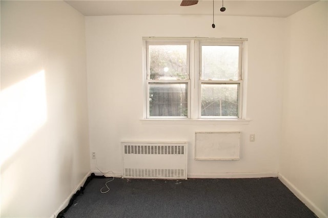 unfurnished room featuring ceiling fan, dark carpet, and radiator