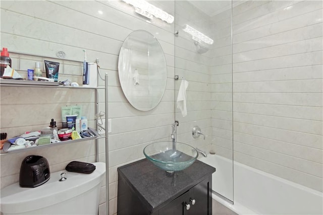 full bathroom featuring tiled shower / bath combo, vanity, toilet, and tile walls