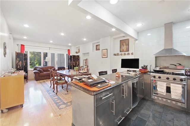 kitchen with wall chimney range hood, dark stone countertops, luxury stove, dark hardwood / wood-style floors, and wine cooler