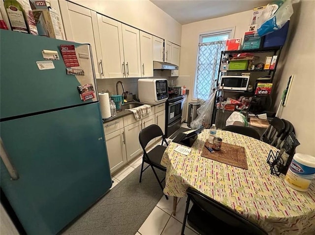 kitchen with refrigerator, sink, white cabinets, light tile patterned floors, and electric range