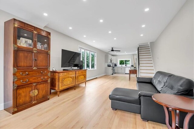 living room with a baseboard heating unit, ceiling fan, and light wood-type flooring