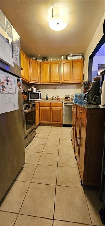 kitchen with light tile patterned floors, stainless steel appliances, brown cabinetry, and a sink