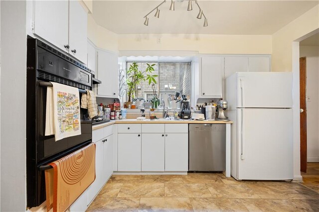 kitchen with stainless steel dishwasher, freestanding refrigerator, a sink, and white cabinets