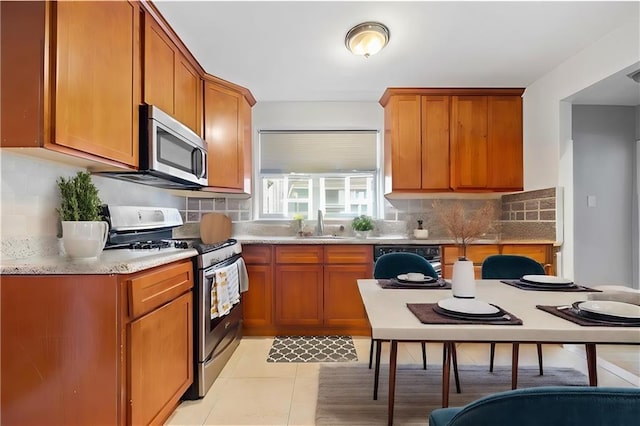kitchen featuring light tile patterned floors, backsplash, stainless steel appliances, and brown cabinets