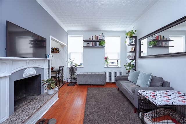 living room with radiator heating unit, a fireplace with raised hearth, and wood finished floors