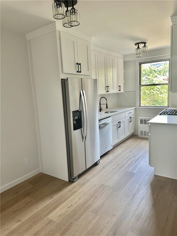 kitchen with appliances with stainless steel finishes, sink, white cabinets, a notable chandelier, and light hardwood / wood-style flooring