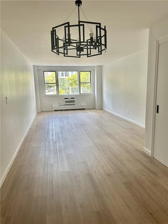 unfurnished dining area with a notable chandelier, baseboards, baseboard heating, and wood finished floors