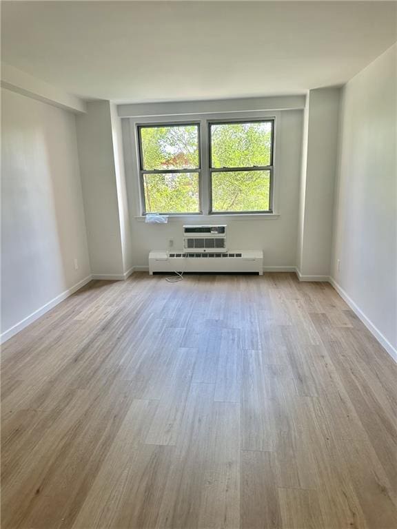 empty room with a wall unit AC, baseboards, and wood finished floors