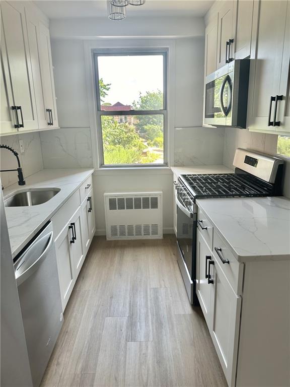 kitchen with a sink, white cabinetry, light wood-style floors, appliances with stainless steel finishes, and radiator heating unit