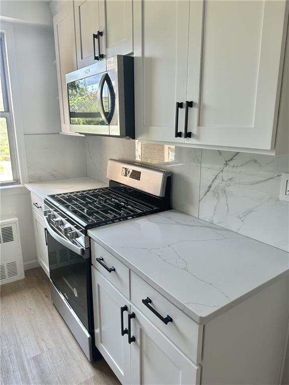 kitchen with white cabinetry, backsplash, light stone counters, light hardwood / wood-style floors, and stainless steel appliances