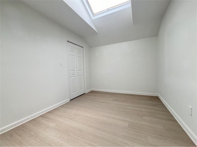 additional living space featuring vaulted ceiling with skylight and light hardwood / wood-style floors