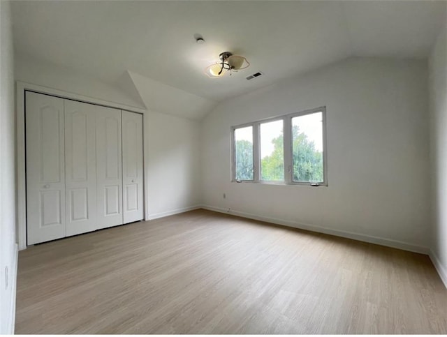 unfurnished bedroom with light wood-type flooring, lofted ceiling, and a closet