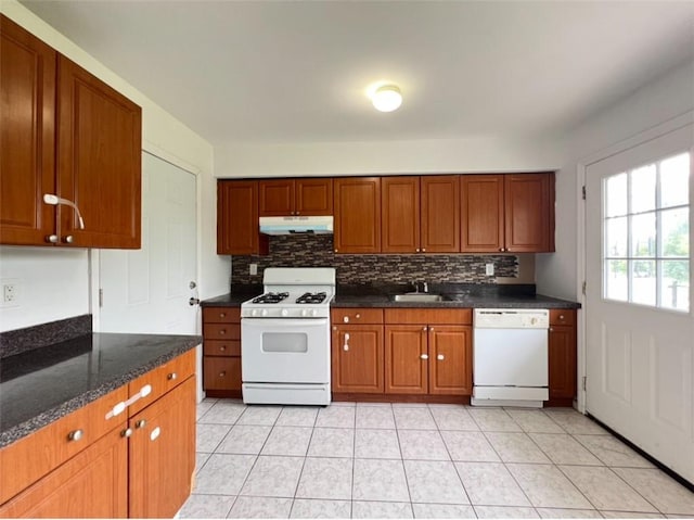 kitchen with decorative backsplash, white appliances, light tile patterned floors, dark stone counters, and sink