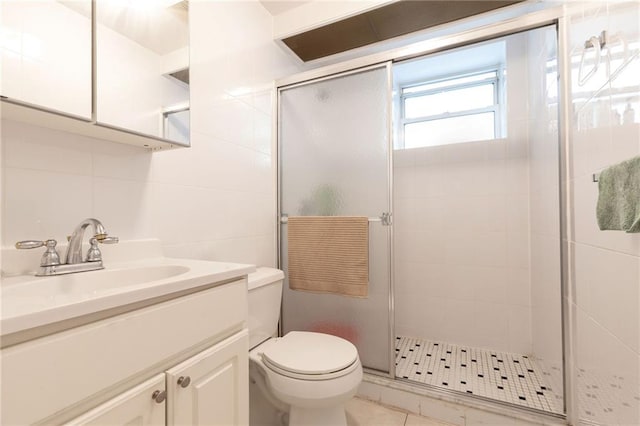 bathroom with tile patterned floors, toilet, vanity, a shower with shower door, and tile walls