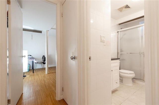 bathroom with toilet, a shower with door, tile walls, and hardwood / wood-style flooring