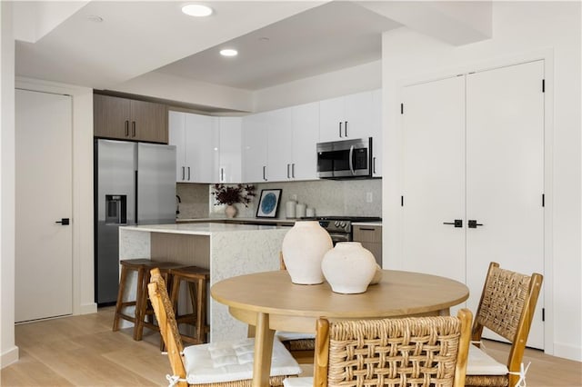 kitchen featuring stainless steel appliances, backsplash, light hardwood / wood-style floors, and white cabinets