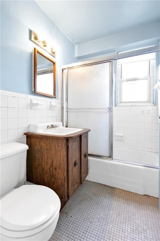 full bathroom featuring toilet, shower / bath combination with glass door, tile walls, vanity, and tile patterned flooring