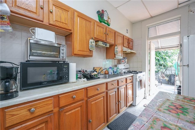 kitchen featuring decorative backsplash, sink, white appliances, and light tile patterned floors