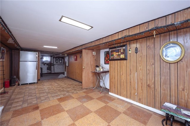 basement with wooden walls, stainless steel refrigerator, and light tile patterned floors