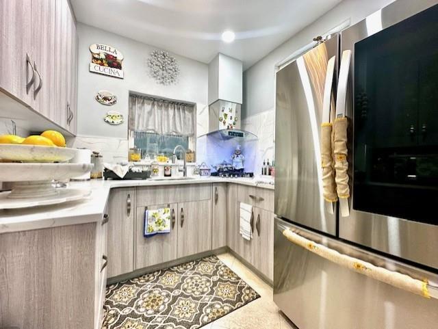 kitchen with stainless steel fridge, sink, light brown cabinets, and wall chimney range hood