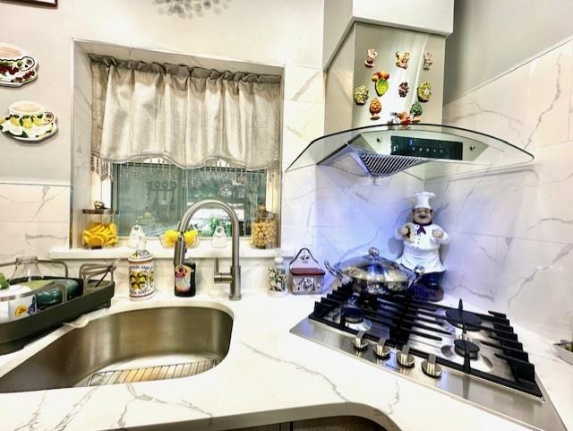 kitchen featuring stainless steel gas stovetop, extractor fan, sink, and tasteful backsplash