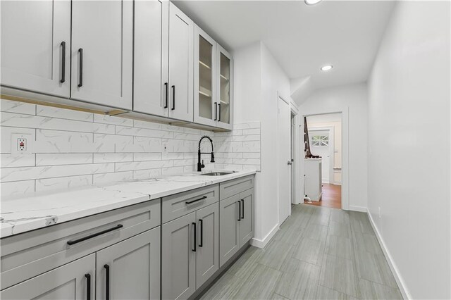 kitchen featuring sink, gray cabinets, backsplash, and light stone counters