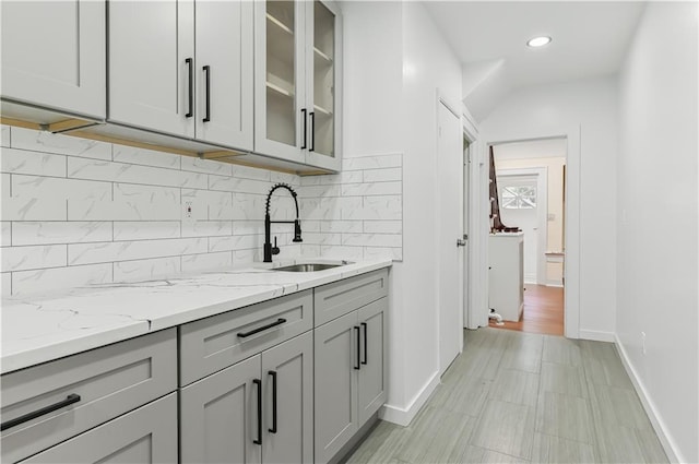 kitchen featuring sink, backsplash, light stone counters, and gray cabinetry