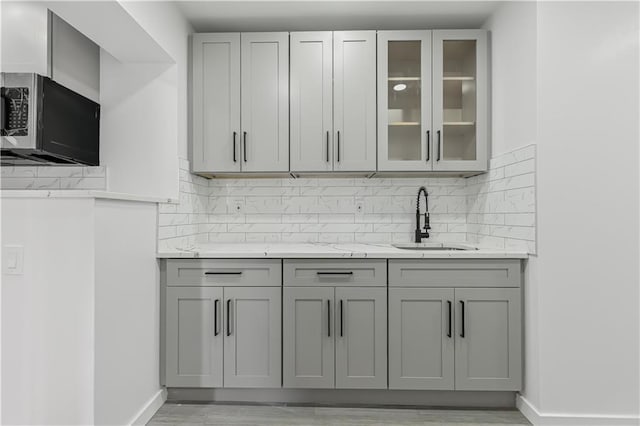 kitchen featuring sink, backsplash, gray cabinetry, and light stone countertops