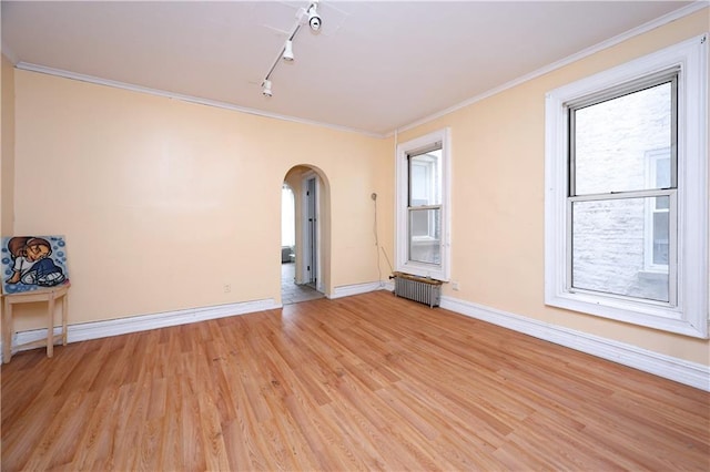 spare room with arched walkways, baseboards, light wood-type flooring, radiator heating unit, and crown molding