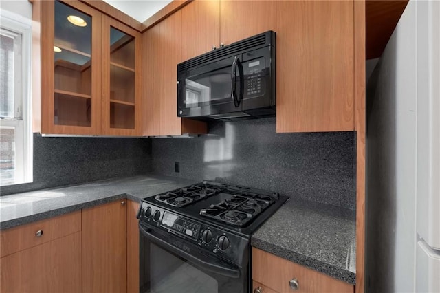 kitchen featuring glass insert cabinets, dark countertops, a healthy amount of sunlight, black appliances, and tasteful backsplash