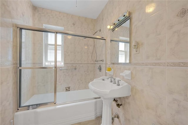 bathroom featuring bath / shower combo with glass door and tile walls