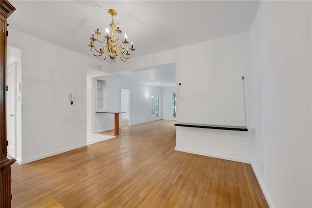 spare room with an inviting chandelier, light wood-style flooring, and baseboards