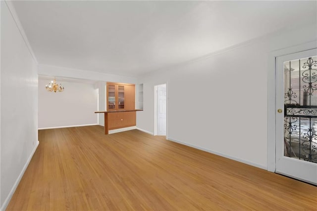 unfurnished living room featuring light wood finished floors, an inviting chandelier, and baseboards
