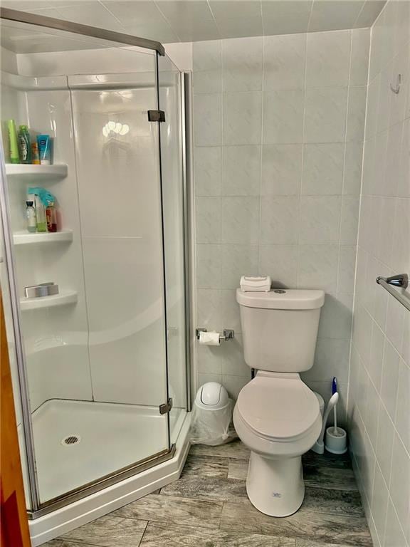 bathroom with tile patterned flooring, tile walls, a shower with shower door, and toilet