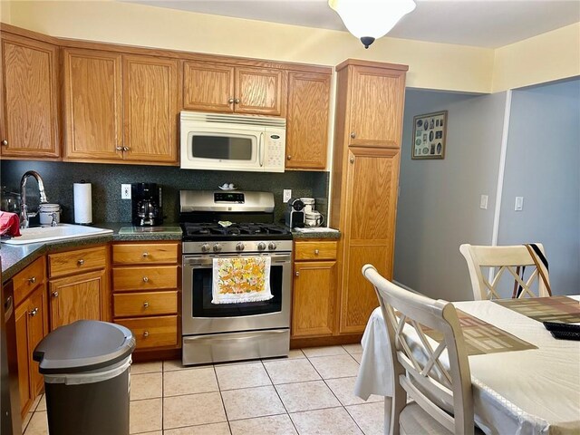 kitchen featuring decorative backsplash, stainless steel gas range oven, light tile patterned floors, and sink