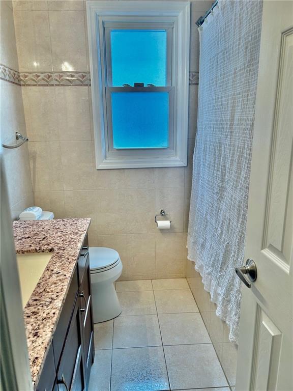 bathroom with tile patterned floors, vanity, tile walls, and toilet