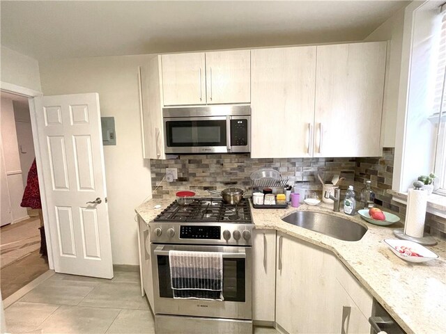 kitchen with light stone counters, appliances with stainless steel finishes, sink, and tasteful backsplash